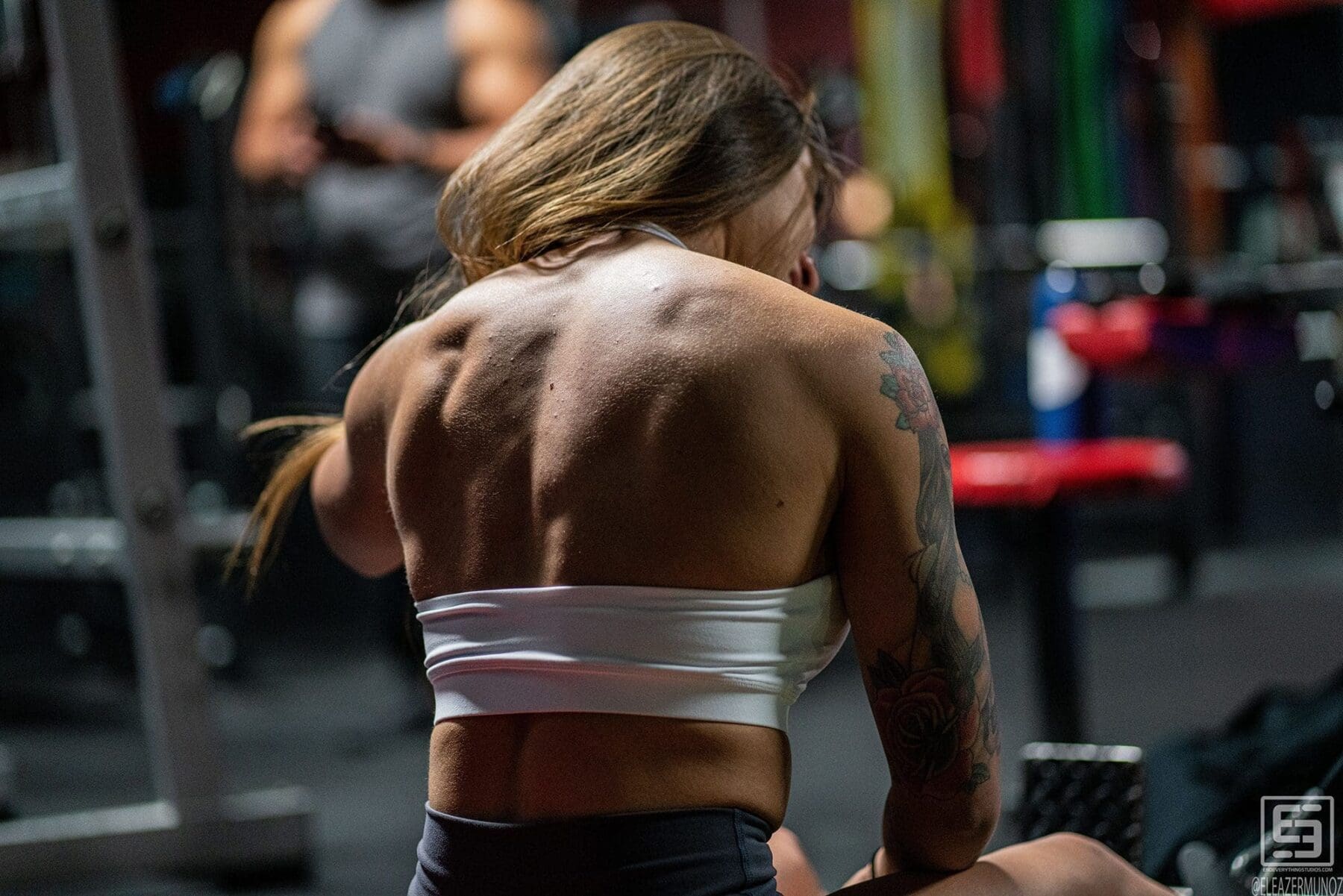 A close rear view shows Danni's back and shoulders as she works at a seated cable station.