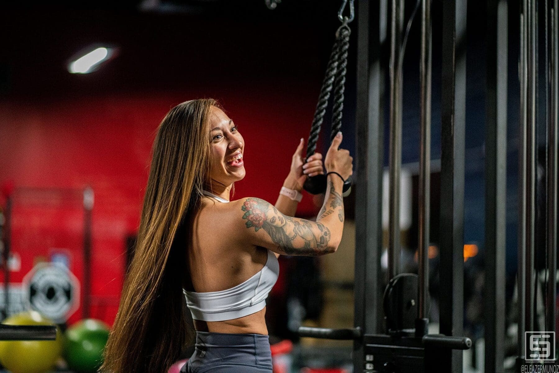 Danni smiles toward the camera while holding a rope attachment at a cable machine.