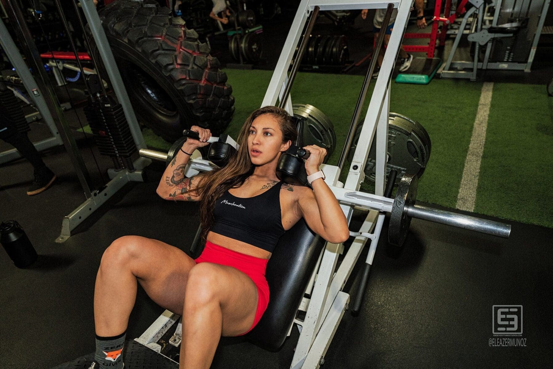 Danni holds two dumbbells at shoulder height while seated against an inclined bench.