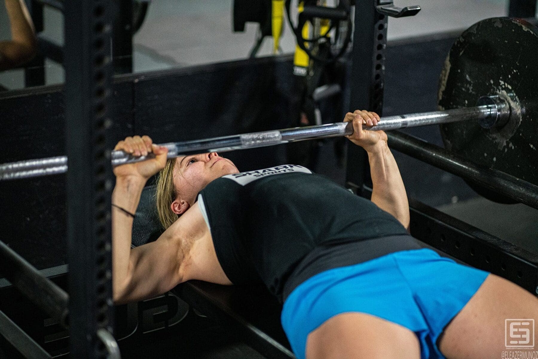 Day presses a barbell from a flat bench in a dramatic low-angle view.