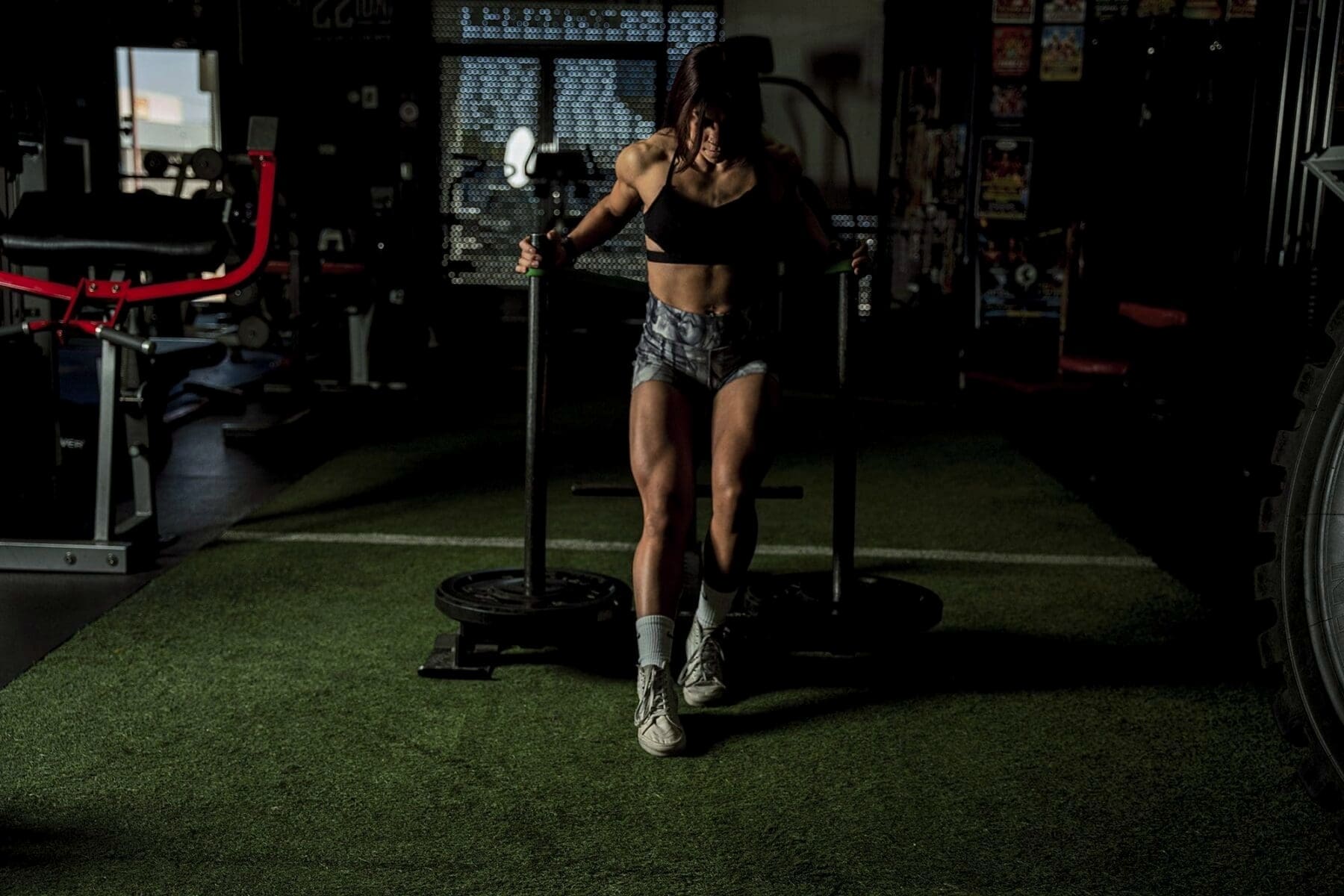Clarissa stands behind a training sled on green indoor turf.