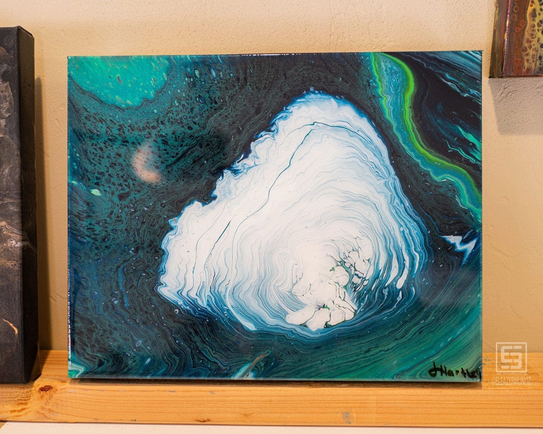 A square abstract artwork features a large white organic form surrounded by teal, green, blue, and black layers.