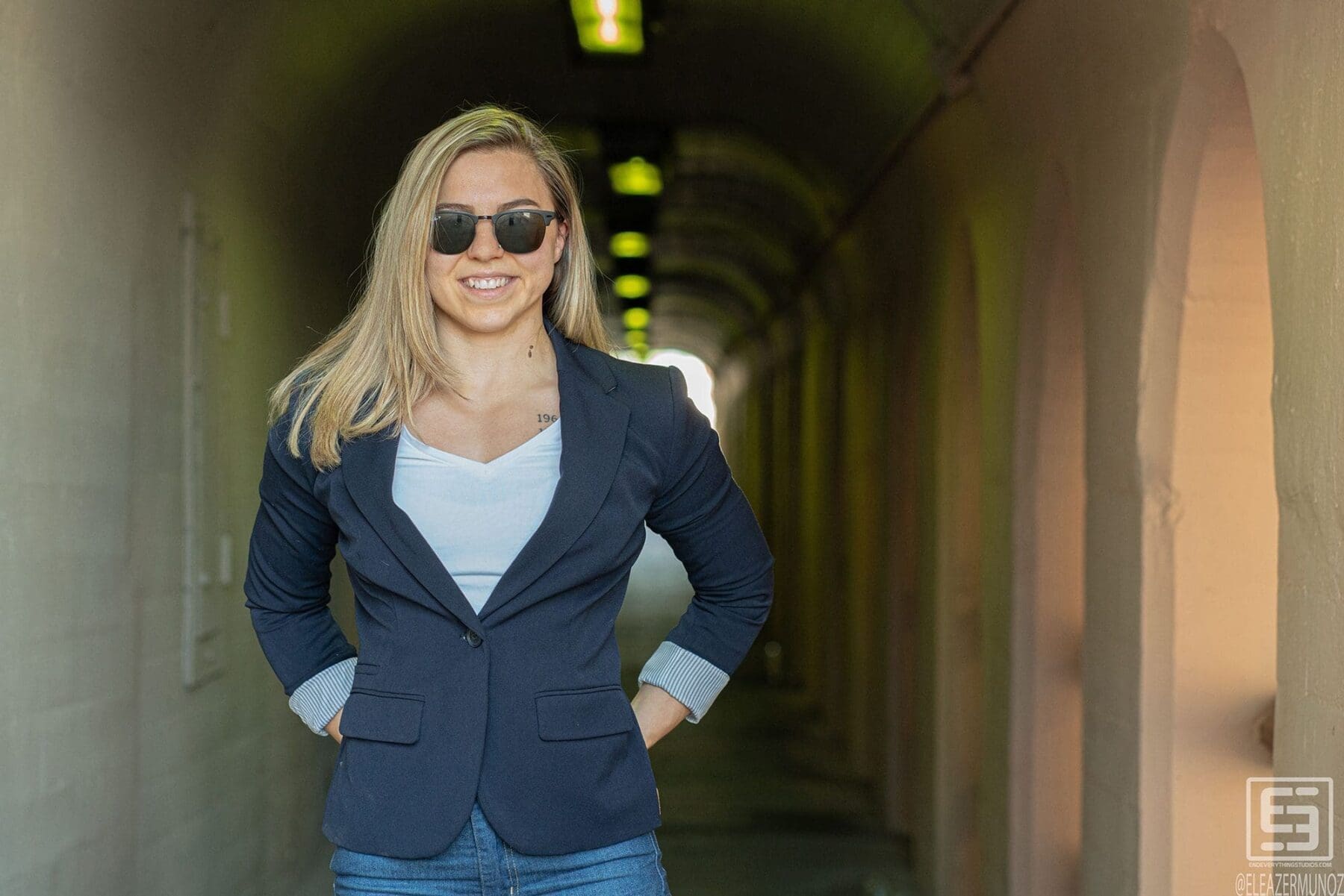Day Muñoz faces the camera without sunglasses in a navy blazer at the entrance to a long arched passage.