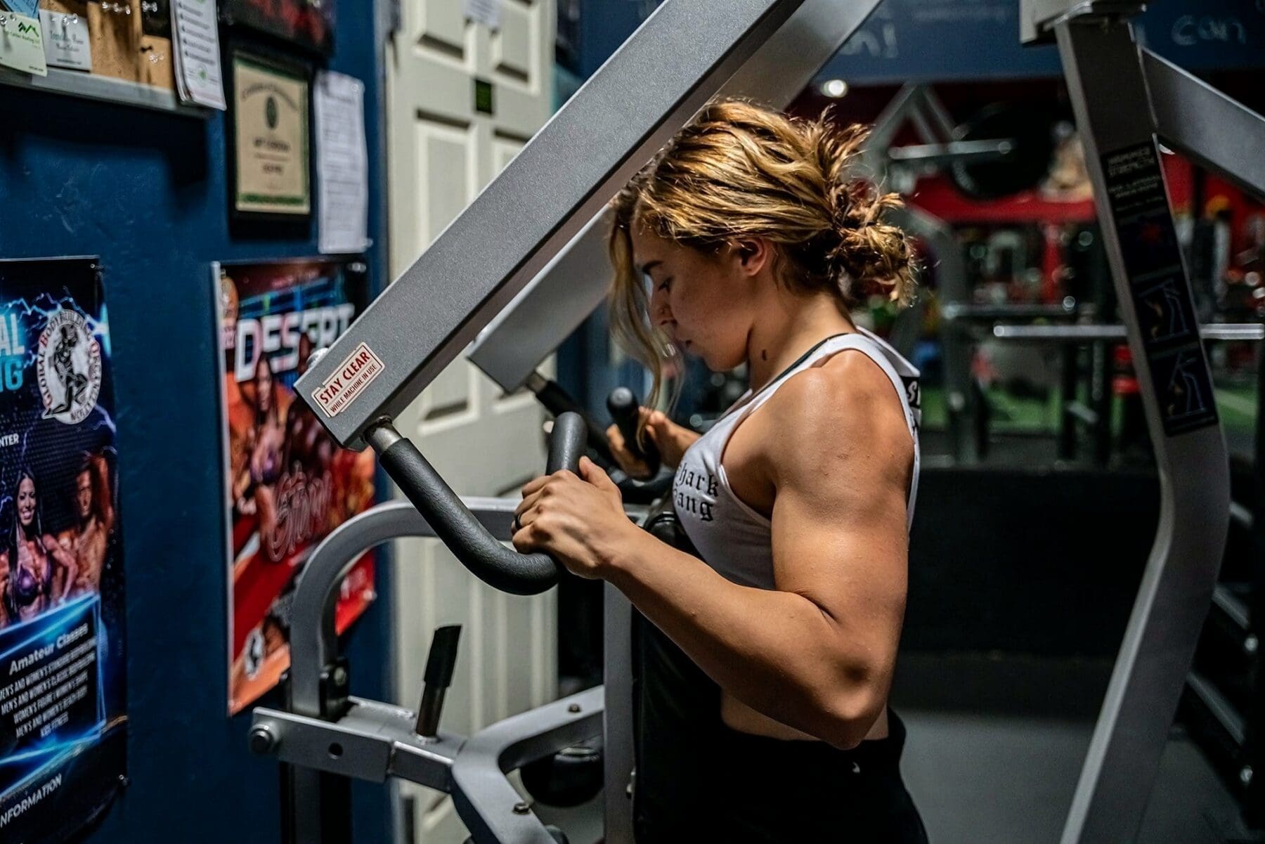 A close side view shows Day working inside a plate-loaded exercise machine.