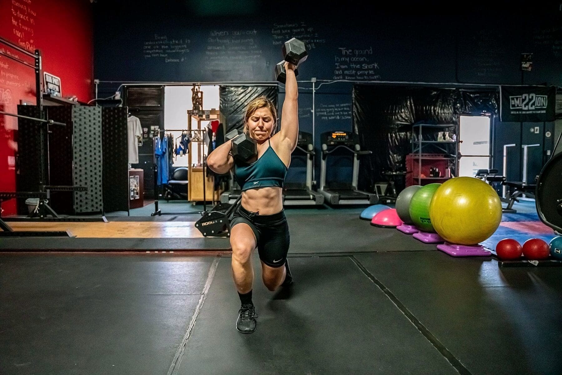 Day presses one dumbbell overhead from a half-kneeling position.