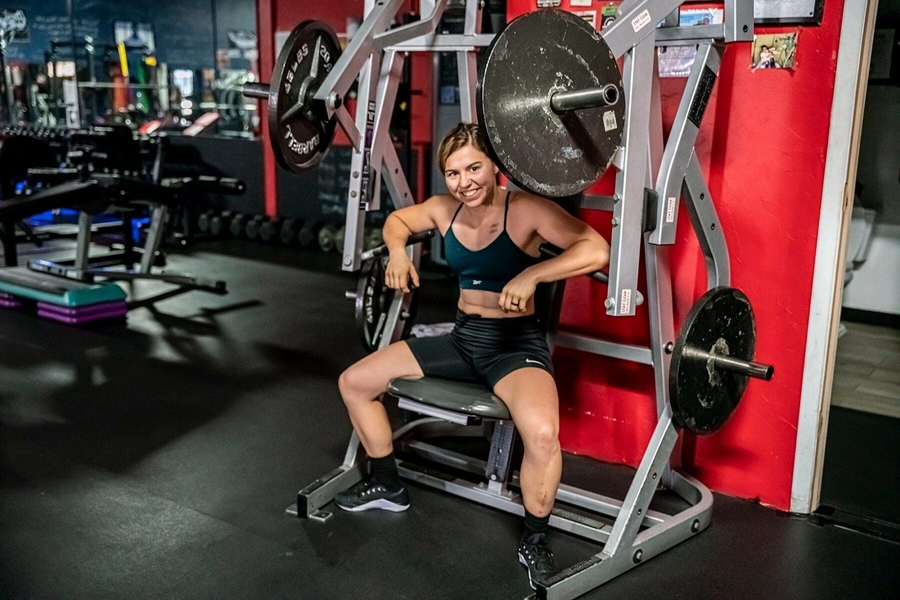 Day smiles while seated beside a plate-loaded machine between exercises.