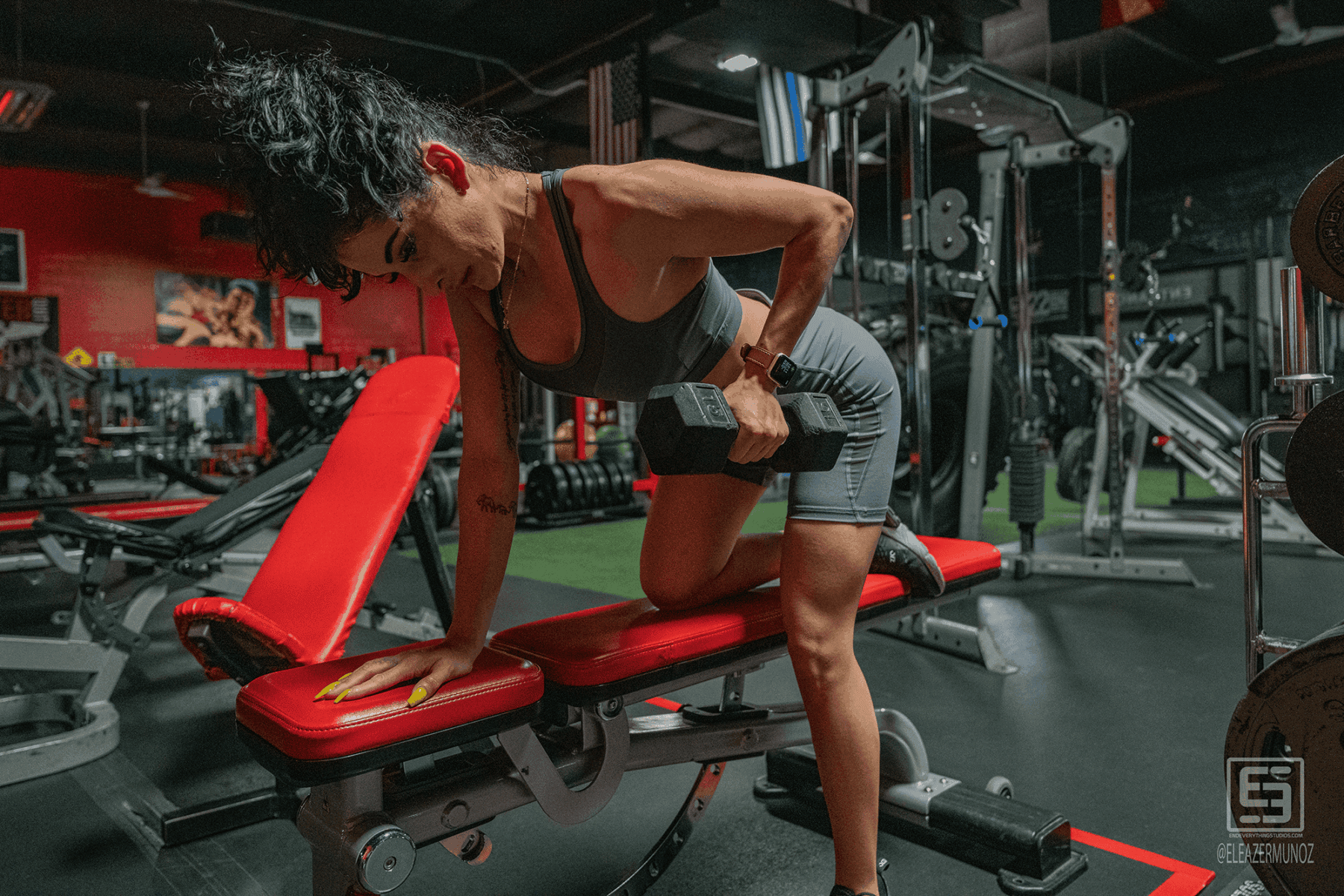 Cynthia performs a one-arm dumbbell row beside a red bench.