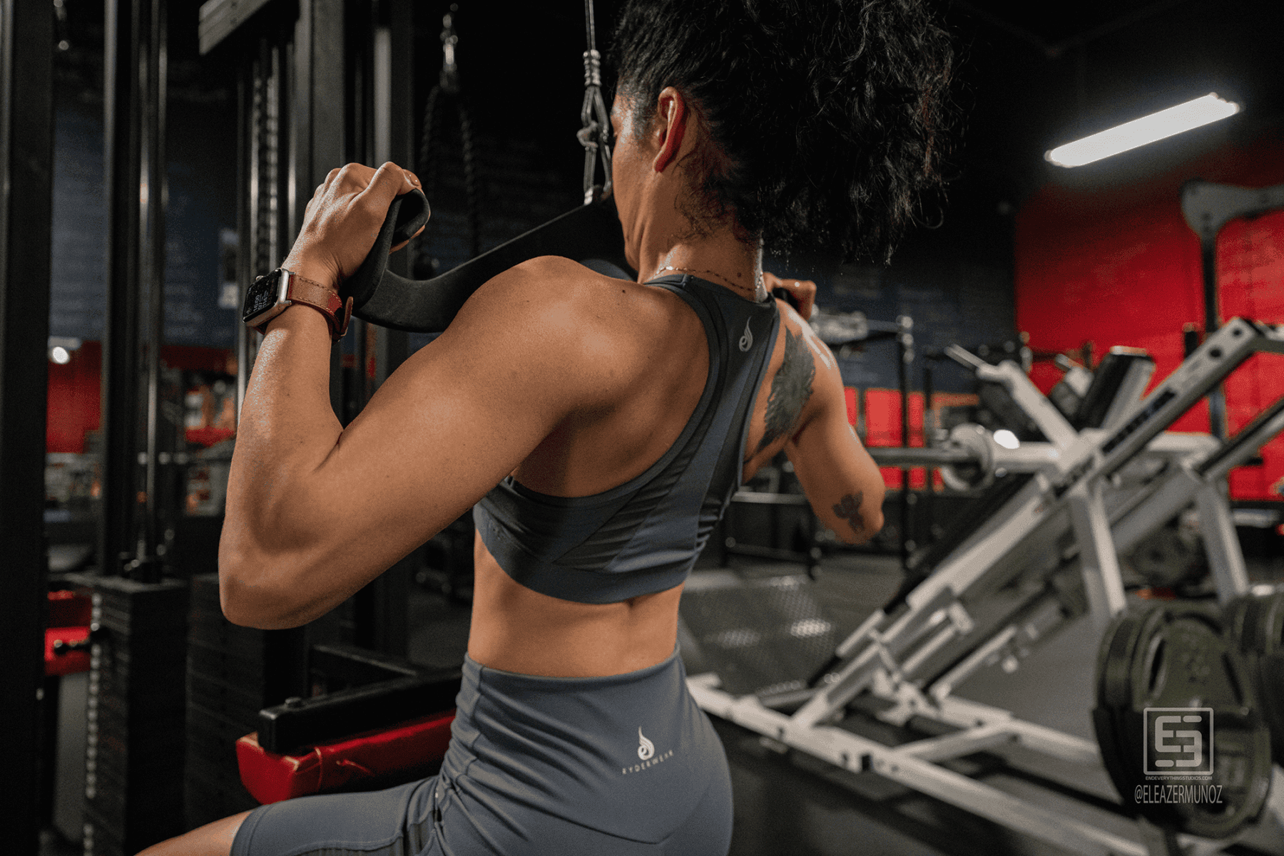 A rear view shows Cynthia pulling cable handles while seated.
