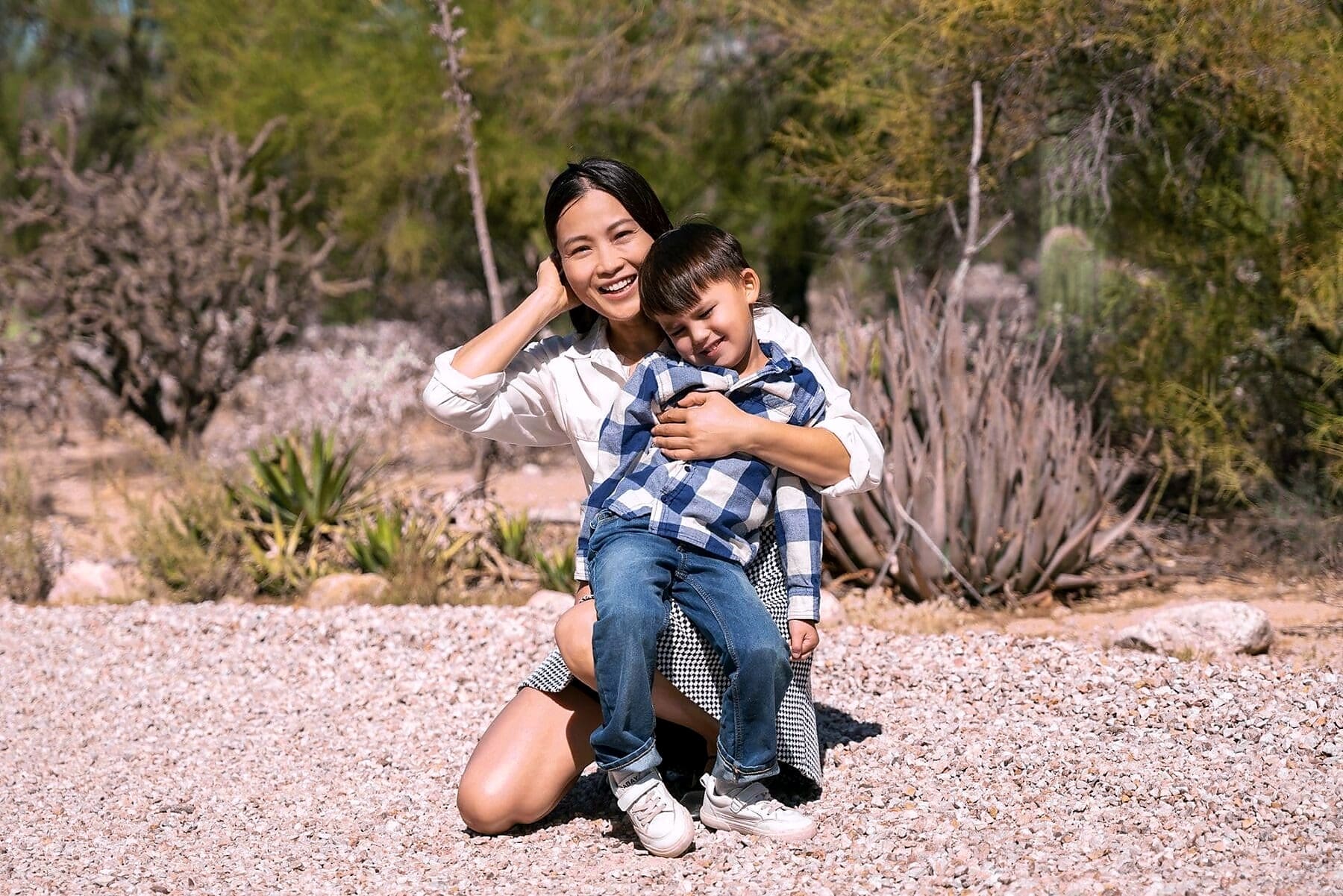 An adult laughs while holding a child close in a sunlit desert garden.