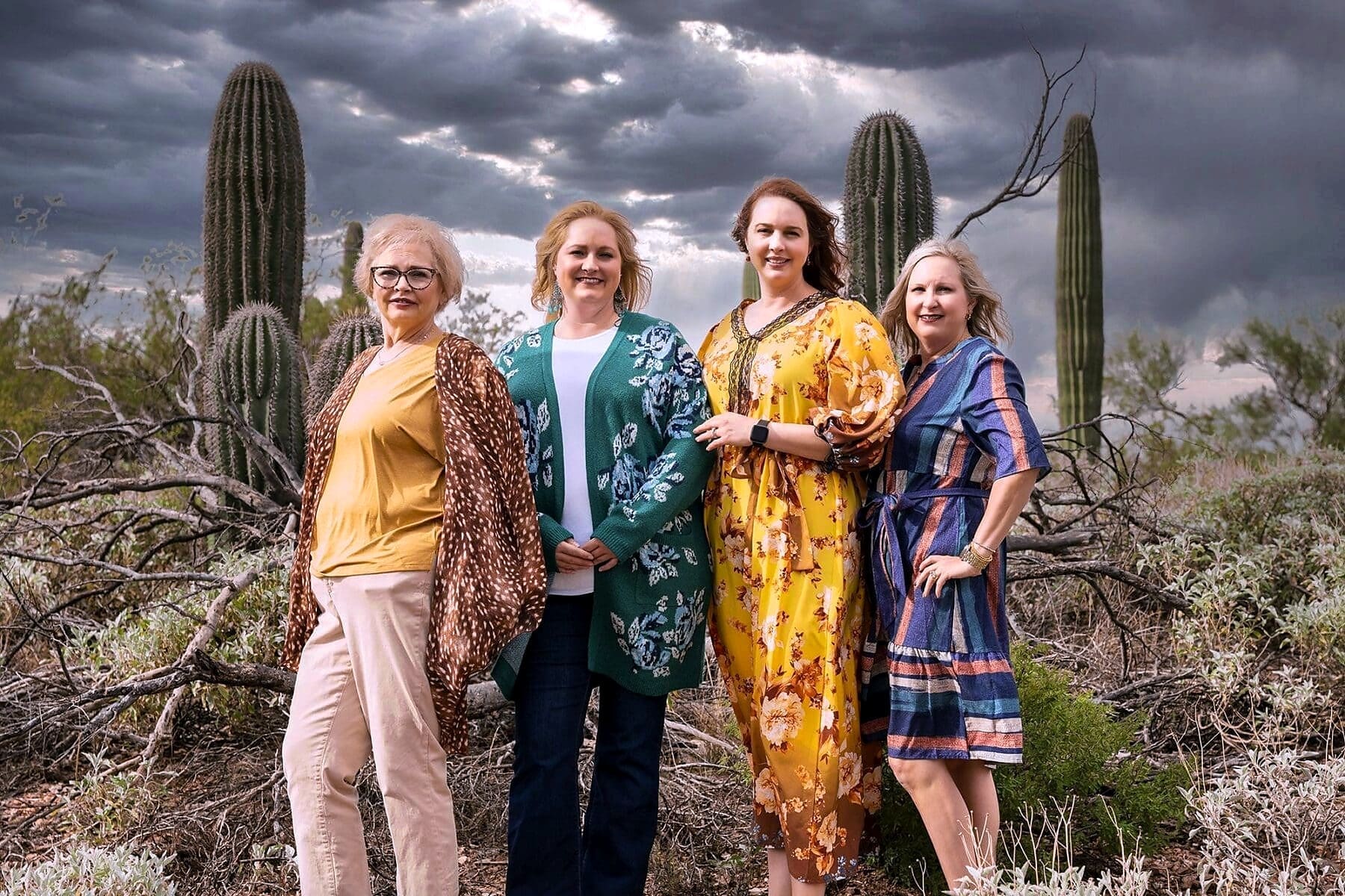 Four women pose together among saguaros with a dark cloud bank behind them.