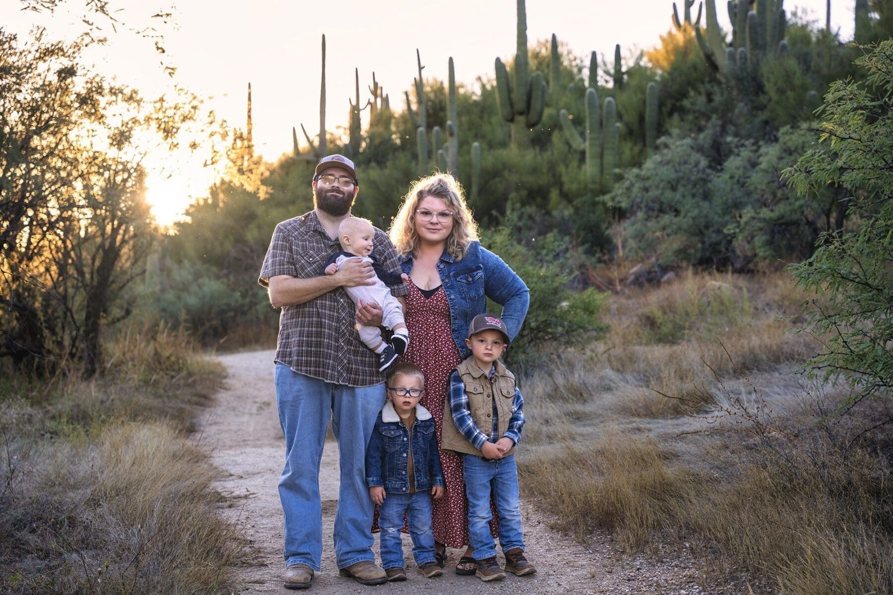 Two adults and three children pose together on a winding path with saguaros and evening light behind them.