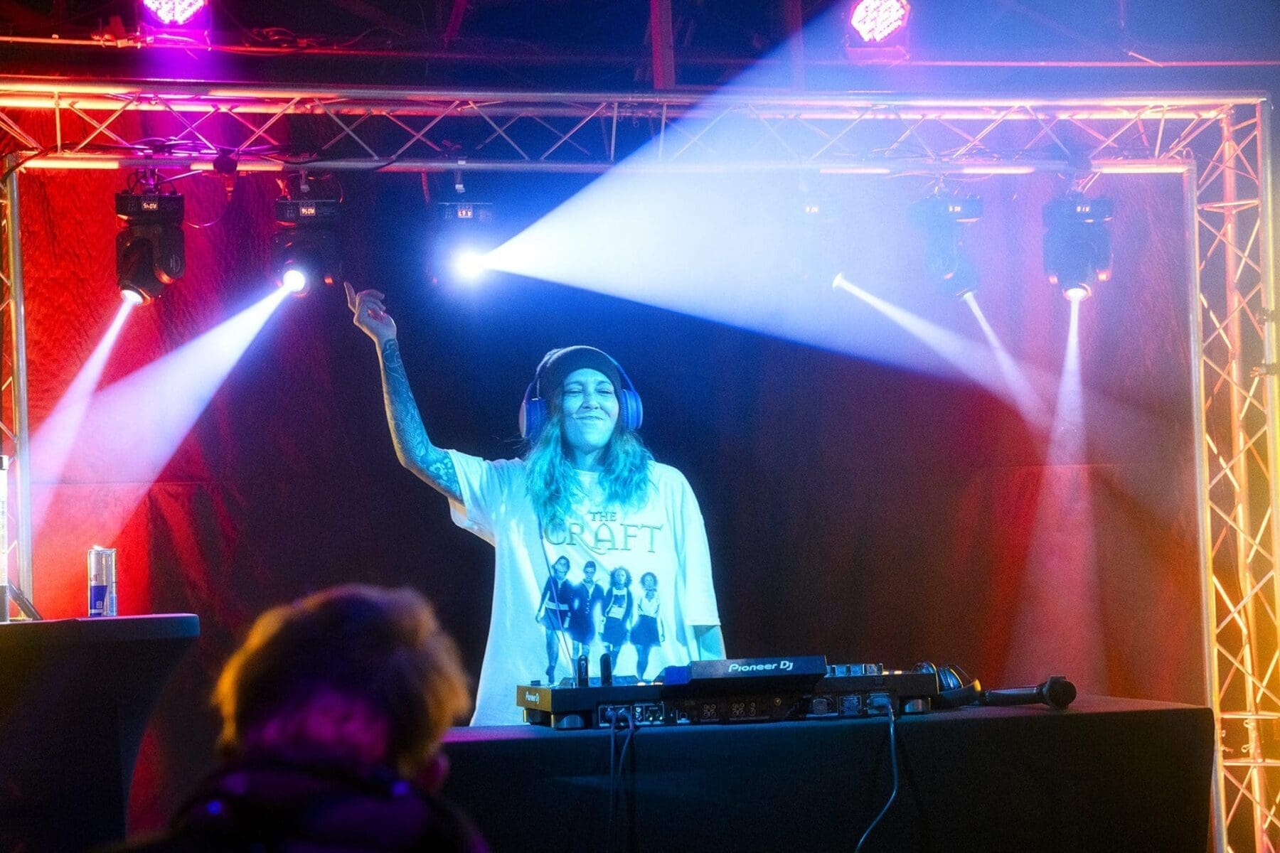 A DJ raises one arm behind the console as the crowd and illuminated cloud fill the room.