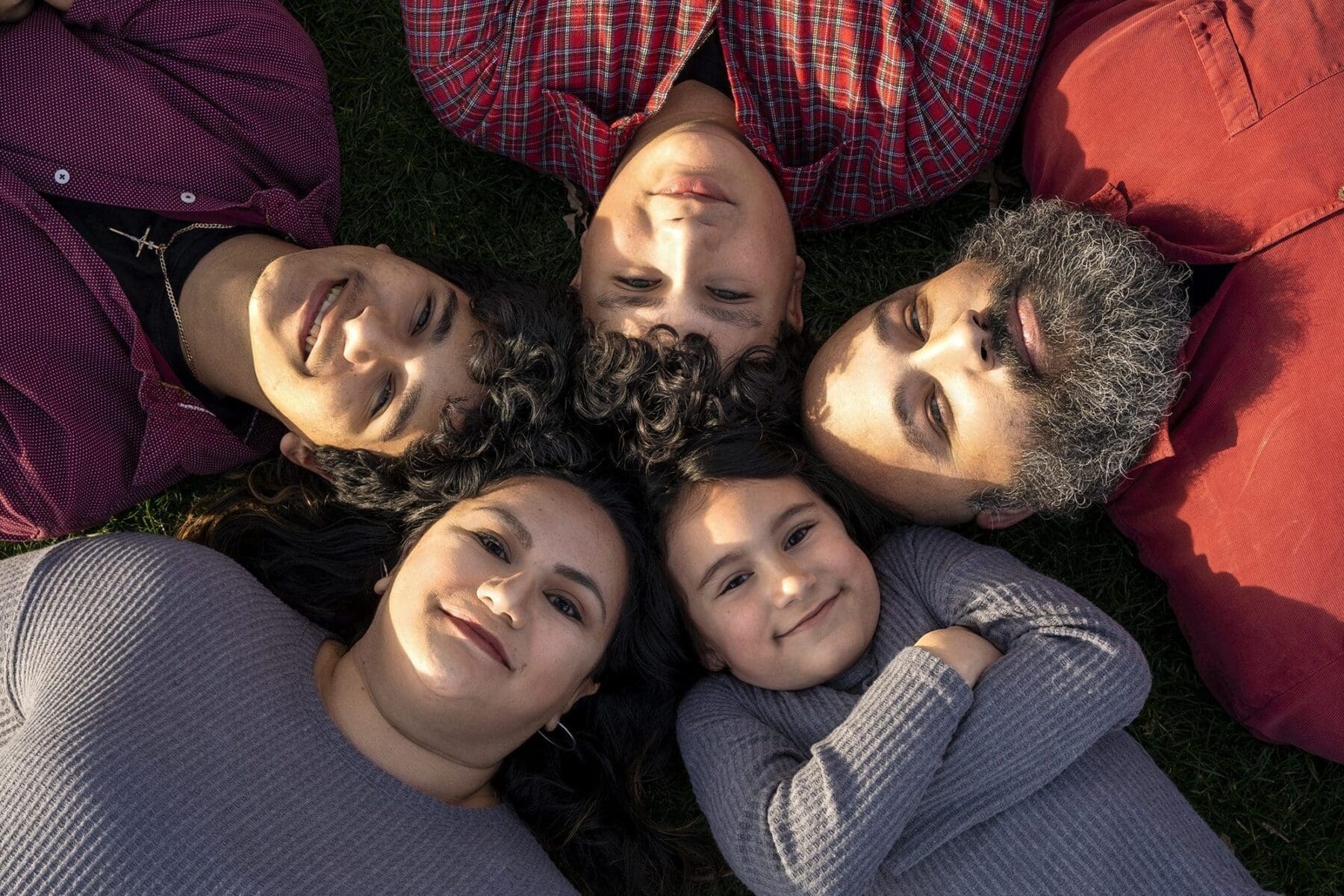 Five family members lie with their heads together in a circle and look up toward the camera.