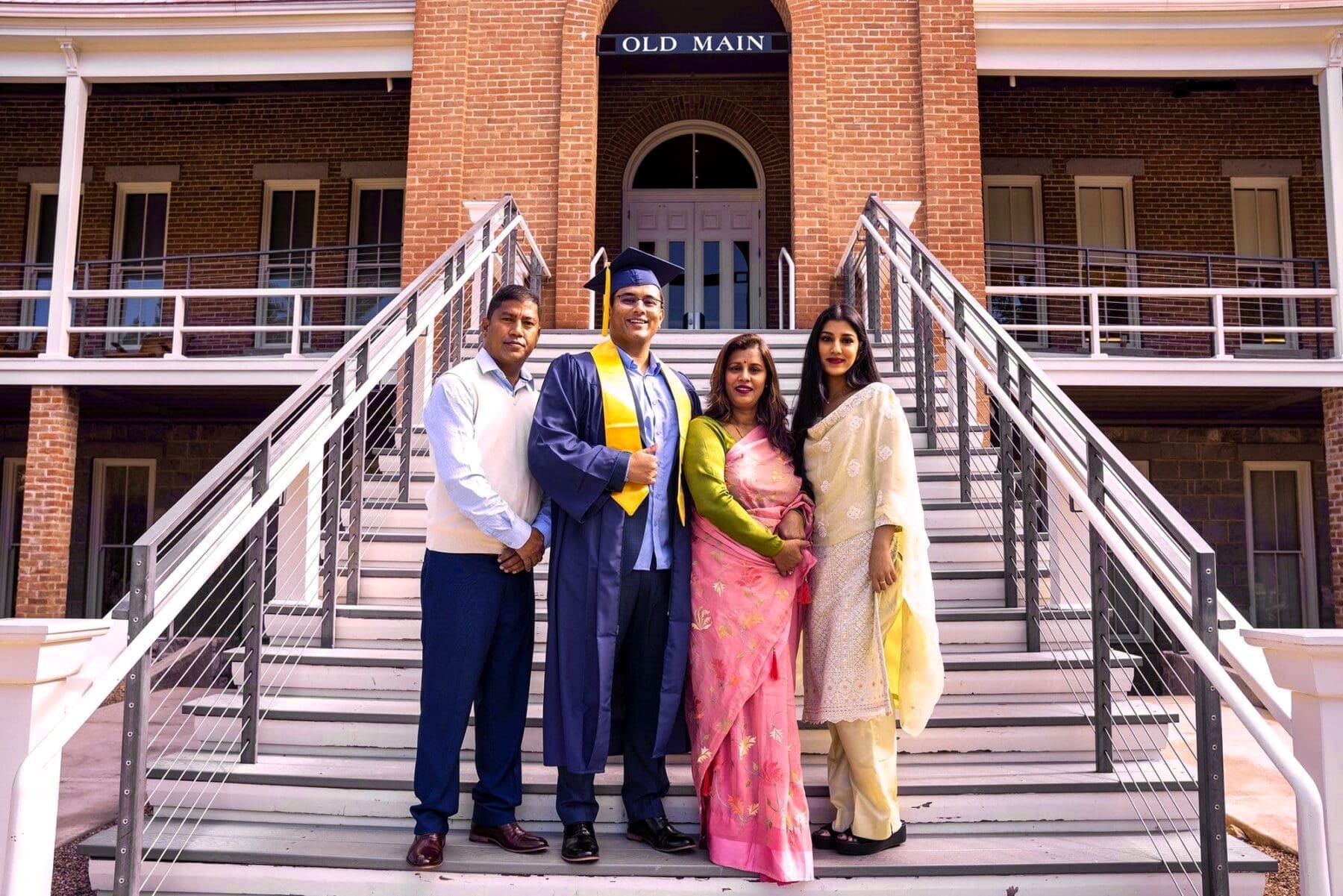 Rehit and three family members pose together on the stairs in front of Old Main.