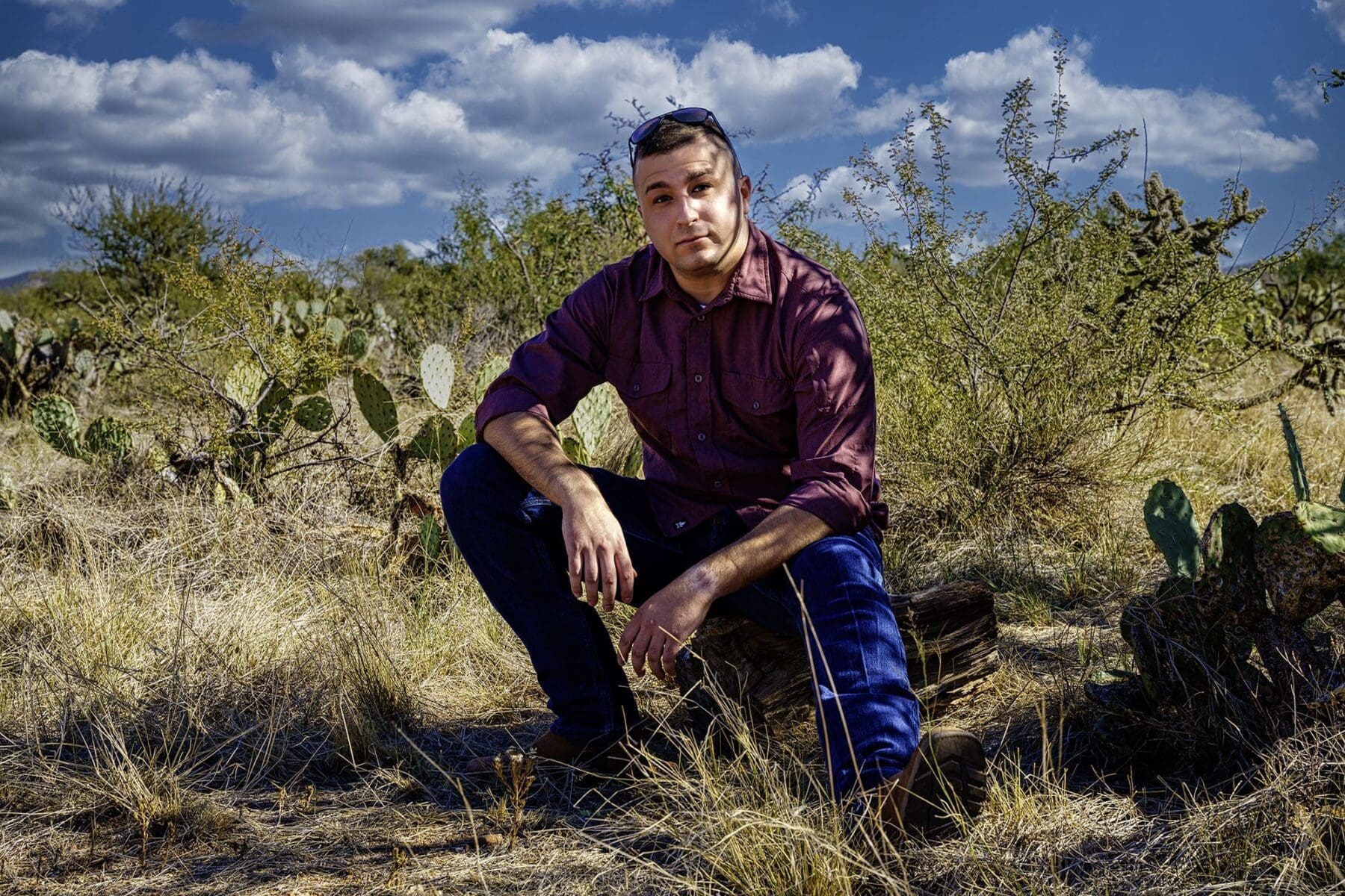 Brandon seated among prickly pear cactus and dry desert grasses in a shaded Tucson portrait