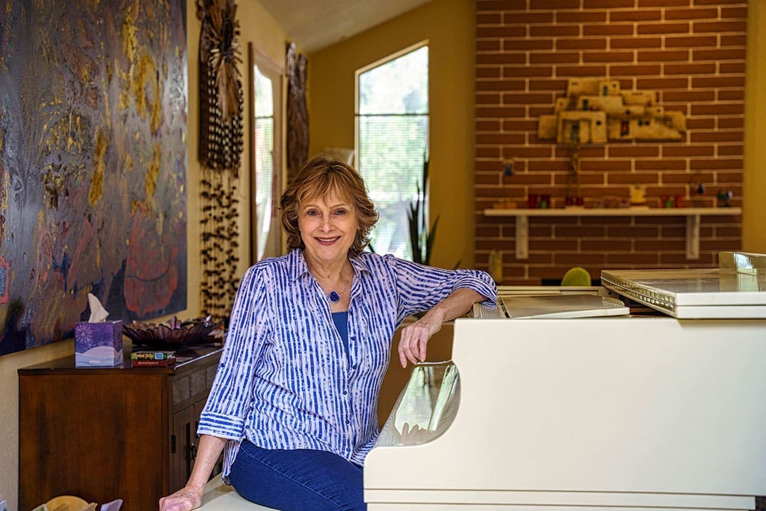 An environmental portrait of Kate seated beside a grand piano and artwork.