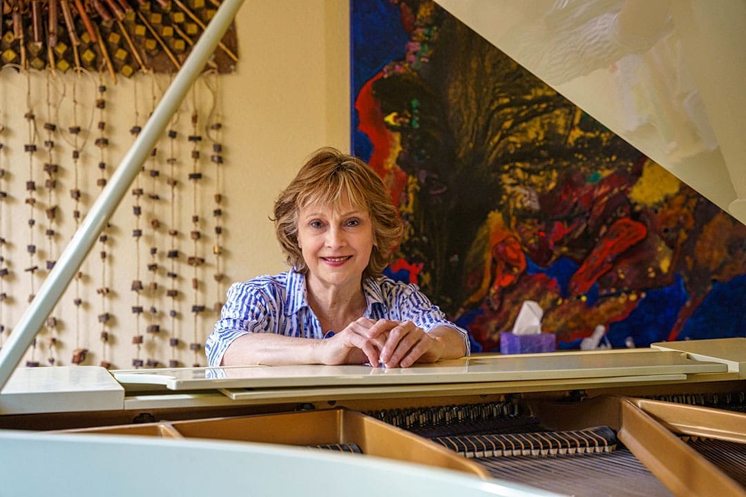 Kate poses beside a grand piano in a colorful, art-filled interior.